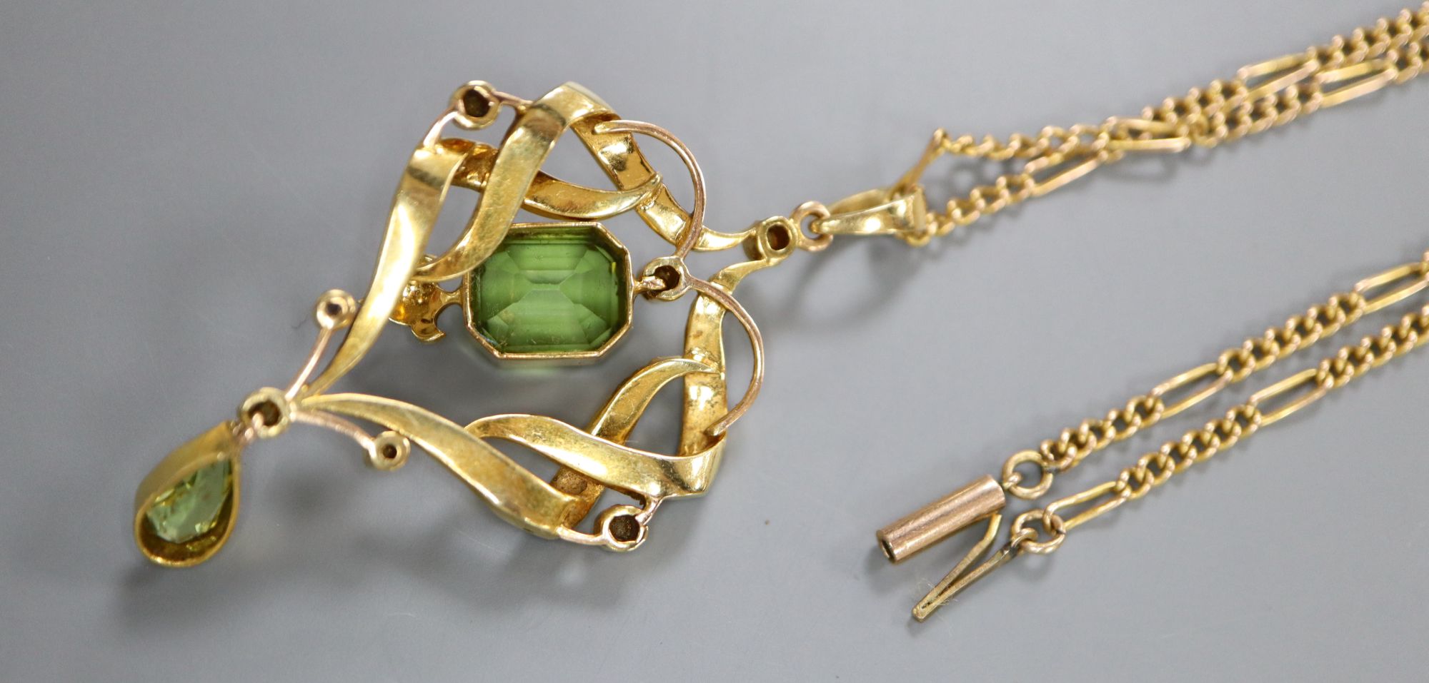 An Edwardian gold, seed pearl and two stone peridot set scroll pendant, overall 53mm, gross 7.4 grams, on 9ct chain.